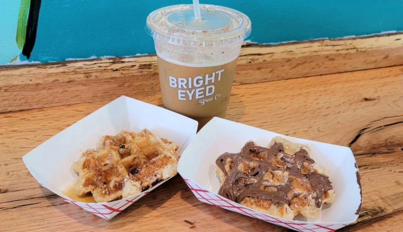 Bright Eyed Brew Co. nitro coffee and two Belgium waffles covered in syrup and nutella.