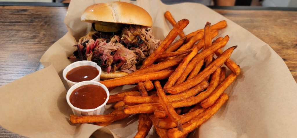 A pulled pork sandwich with sweet potato fries and barbecue sauce on the side at Hog Wild BBQ in downtown Gulf Shores.