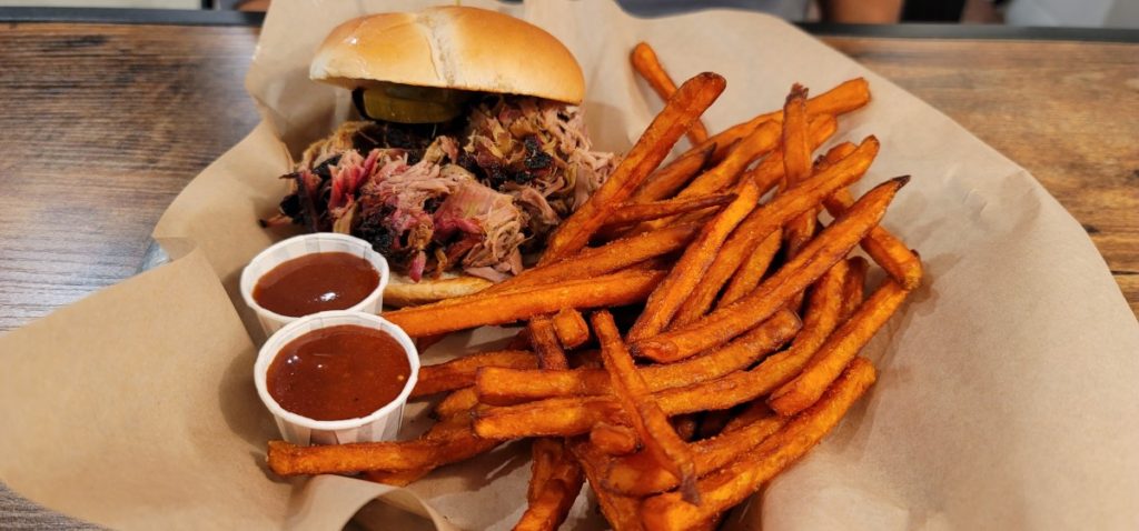 A pulled pork sandwich with sweet potato fries and barbecue sauce on the side at Hog Wild BBQ in downtown Gulf Shores.