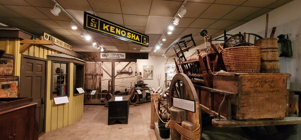 Early Kenosha days including an oxcart, railroad depot, post office, General Store, one room school, blacksmith shop, and a barbershop.