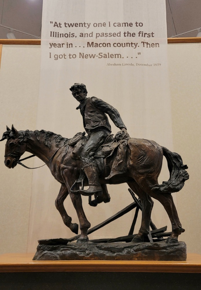 A bronze statue at Lincoln's New Salem museum. The scroll reads, "At twenty one I came to Illinois and passed the first year in... Macon county. Then I got to New-Salem..." December 1859