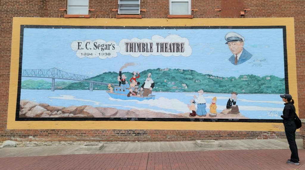 A colorful mural with the cast of the Popeye cartoon in a boat on the Mississippi River in memory of their creator, E.C. Segar's.