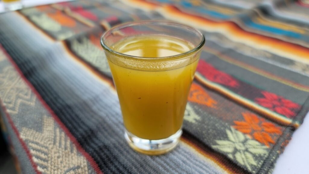 A shot glass filled with the yellow spiced drink of canelazo, a traditional beverage popular in Ecuador.