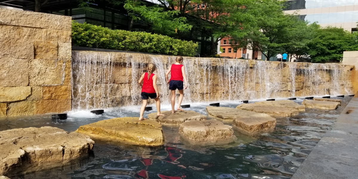 Kids walking along a water feature in the Citygarden Sculpture Park.
