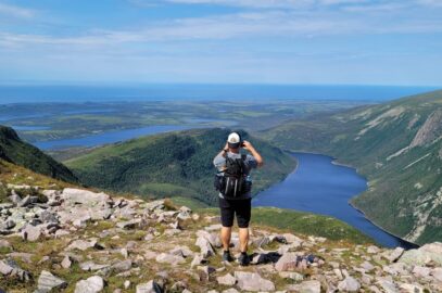 A hiker taking a picture from the summit, taking in the view of the glacial-carved valley at Gros Morne National Park.