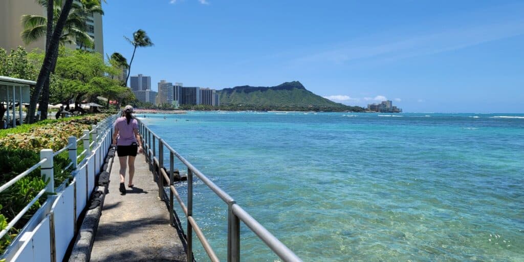 A girl walking the Fort DeRussy Boardwalk along the clear blue water of Honolulu.