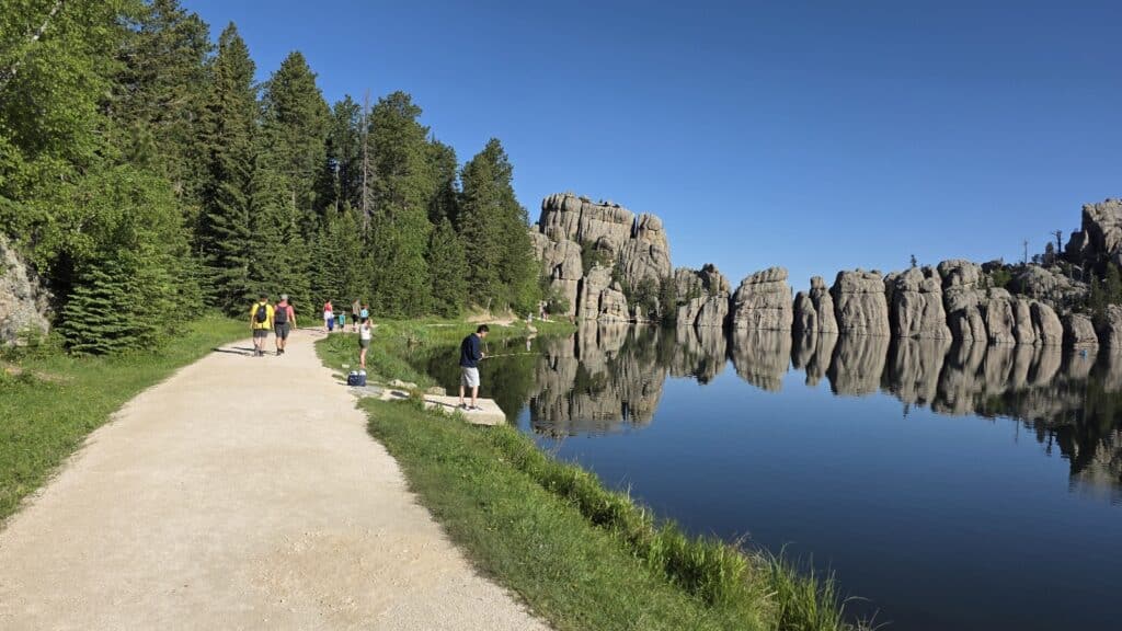 A walking path right along a lake with big boulders being reflected in the water.
